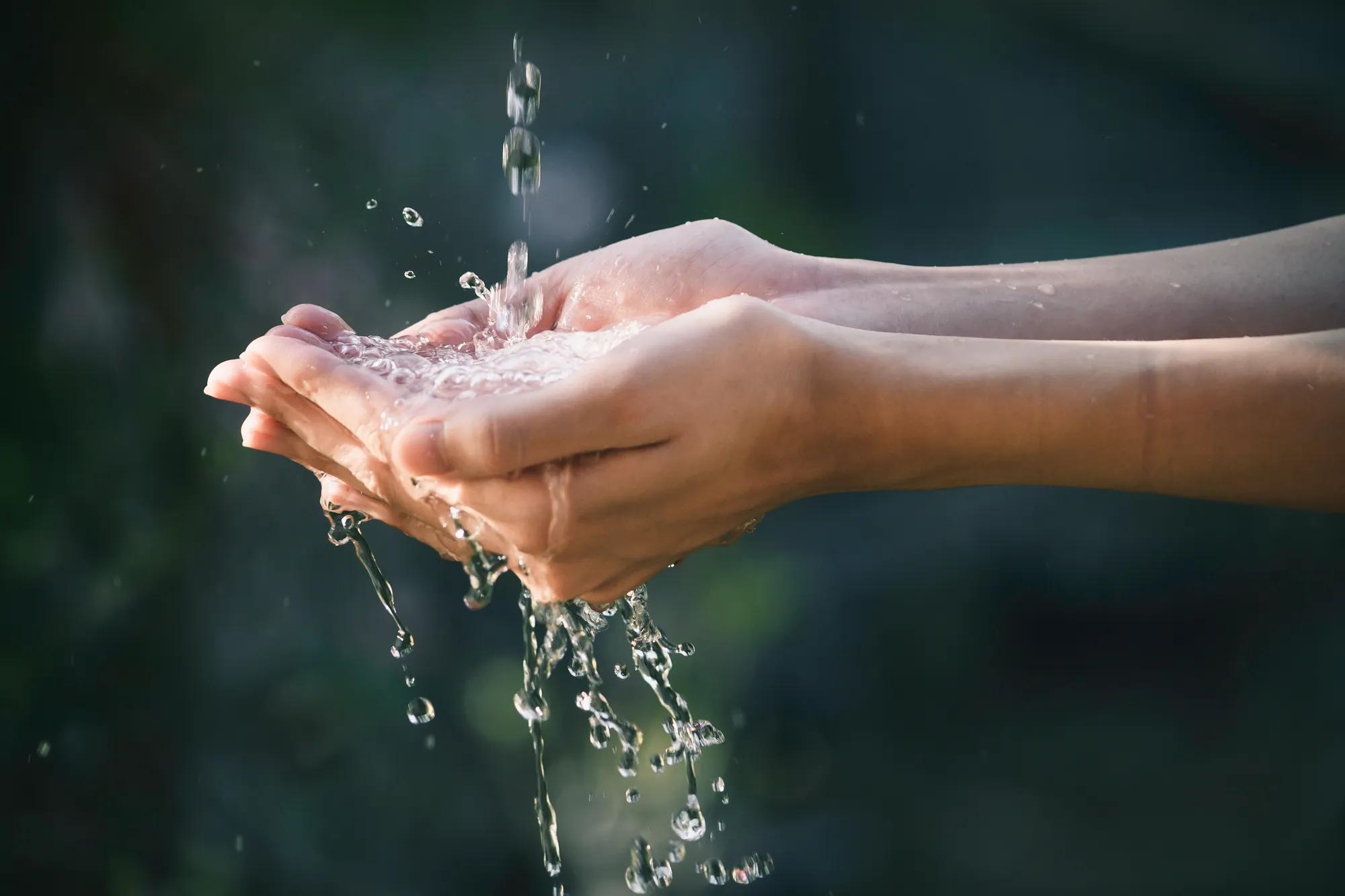 closeup water flow to hand of women for nature concept on the garden background.

