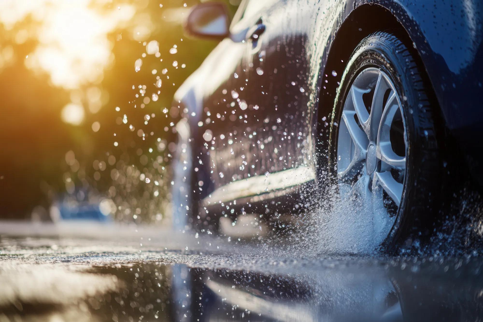 Close-up of car tire splashing water while driving on wet road at sunset