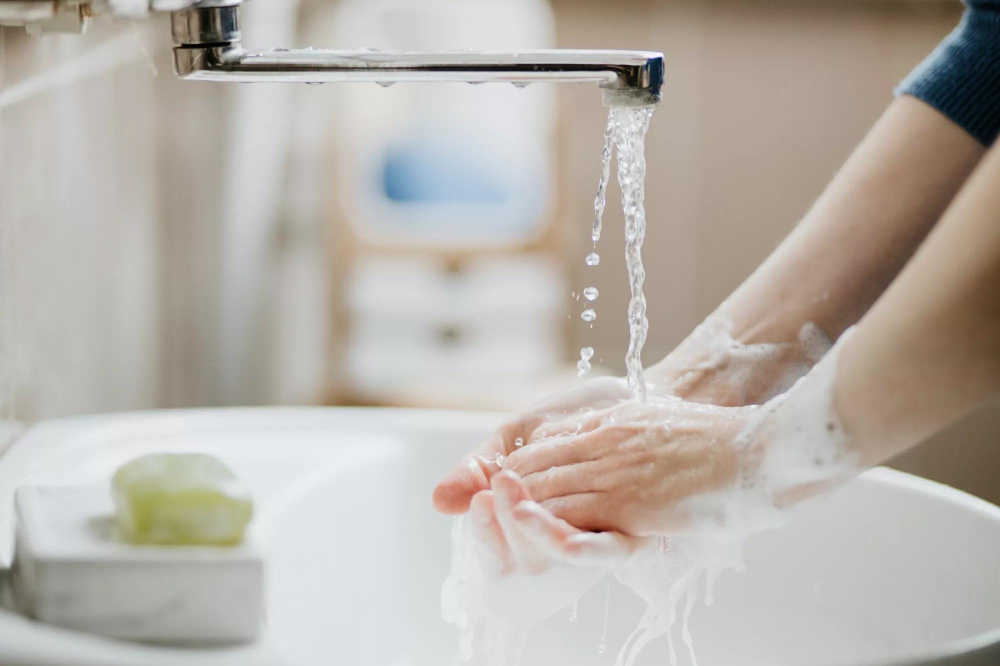 Closeup of a woman washing her hands in bathroom to prevent Covid-19 viral infection. Recommended washing with soap and running water during coronavirus pandemic.