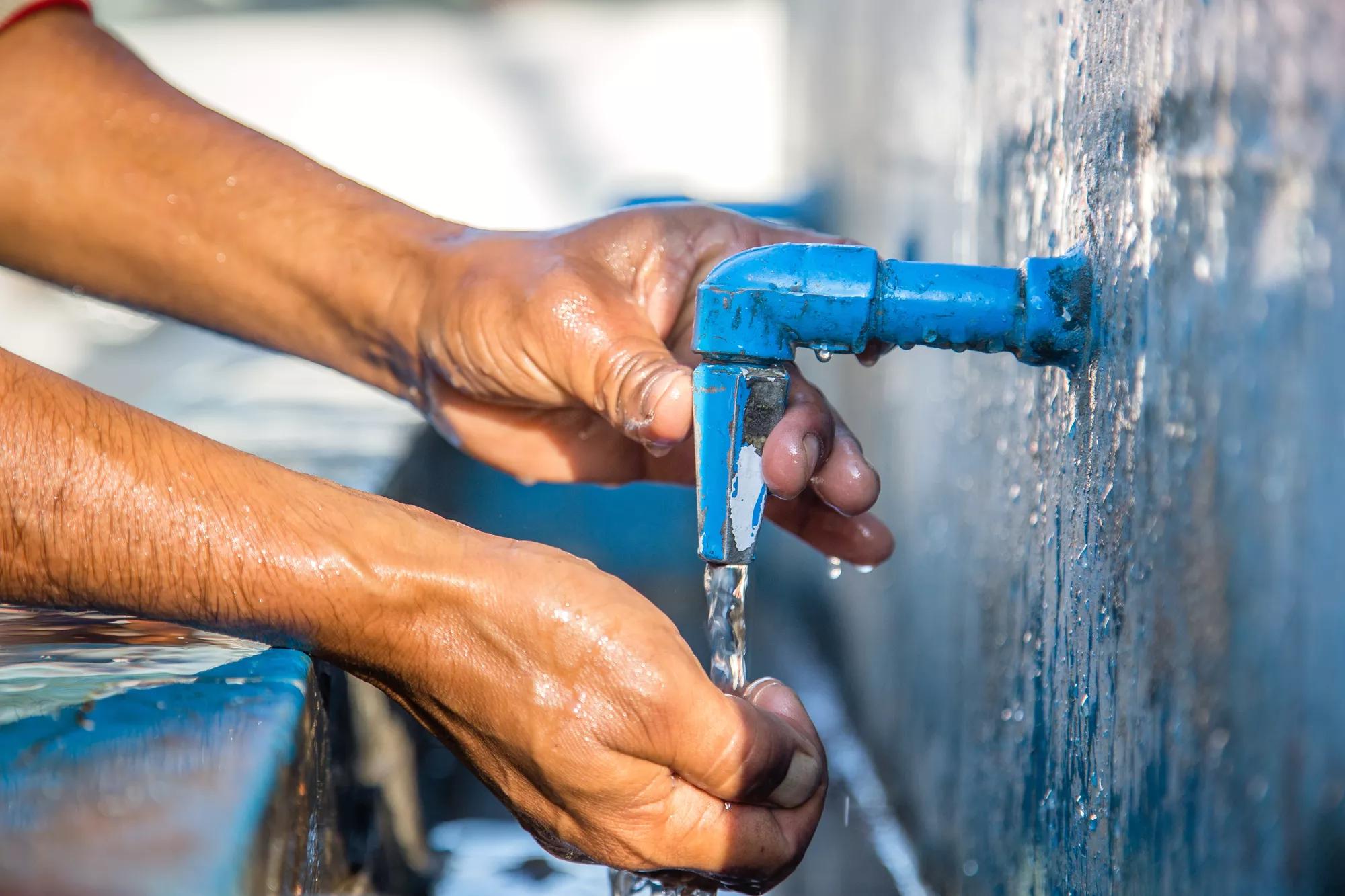 Indian man drinking water from public faucet