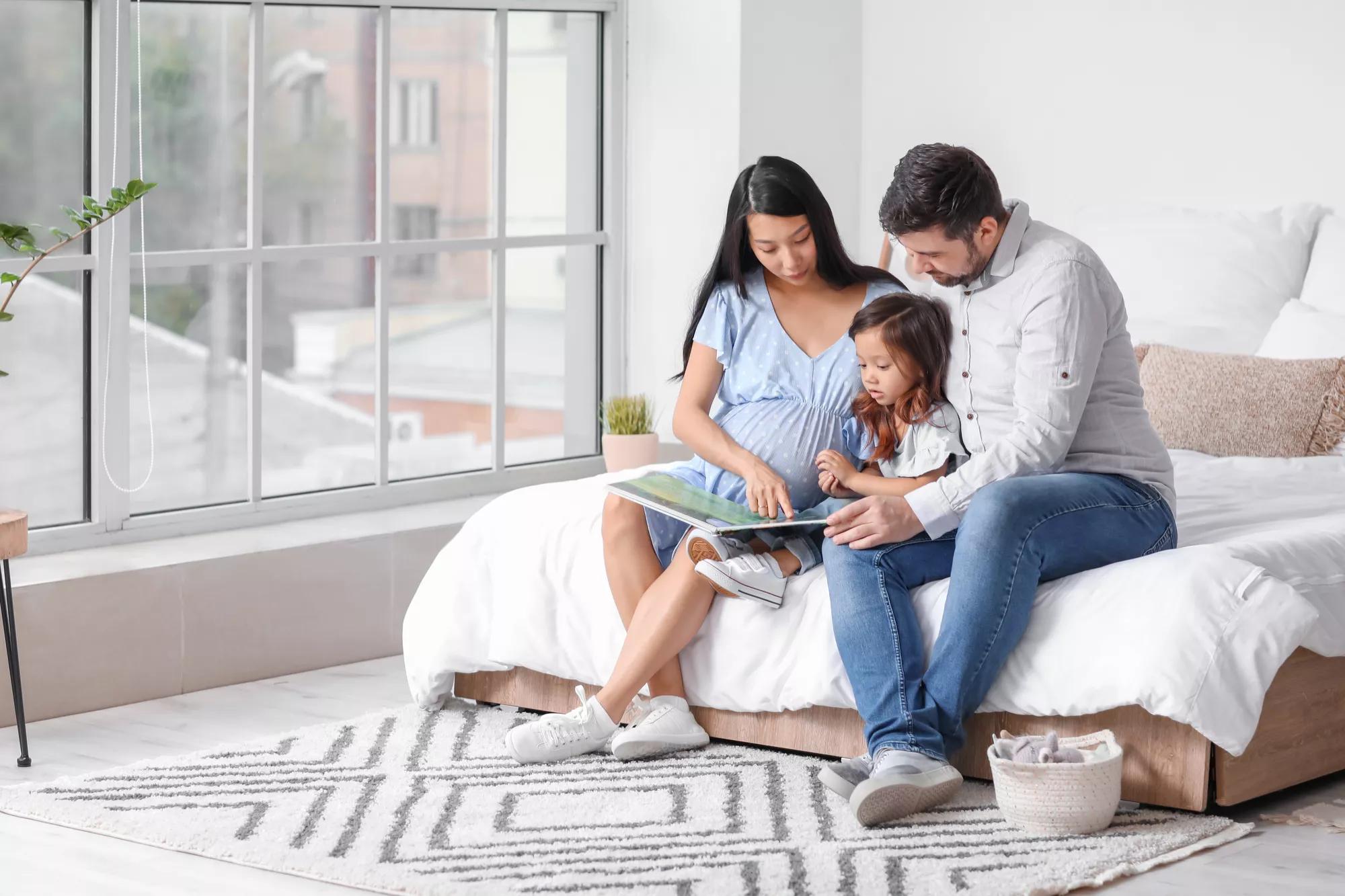 Pregnant Asian woman with her family reading book at home