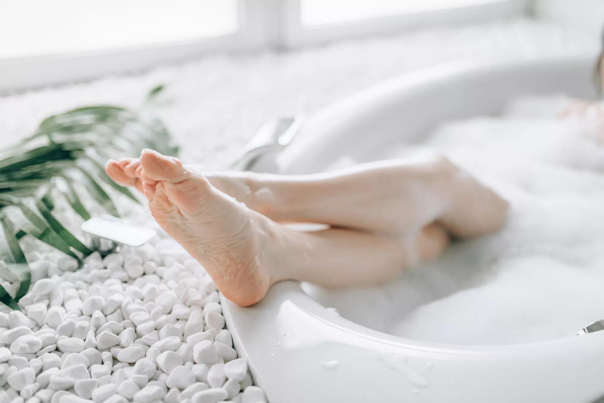 Female person heels sticking out of the bath with foam. Relaxation, health and body care in bathroom, spa