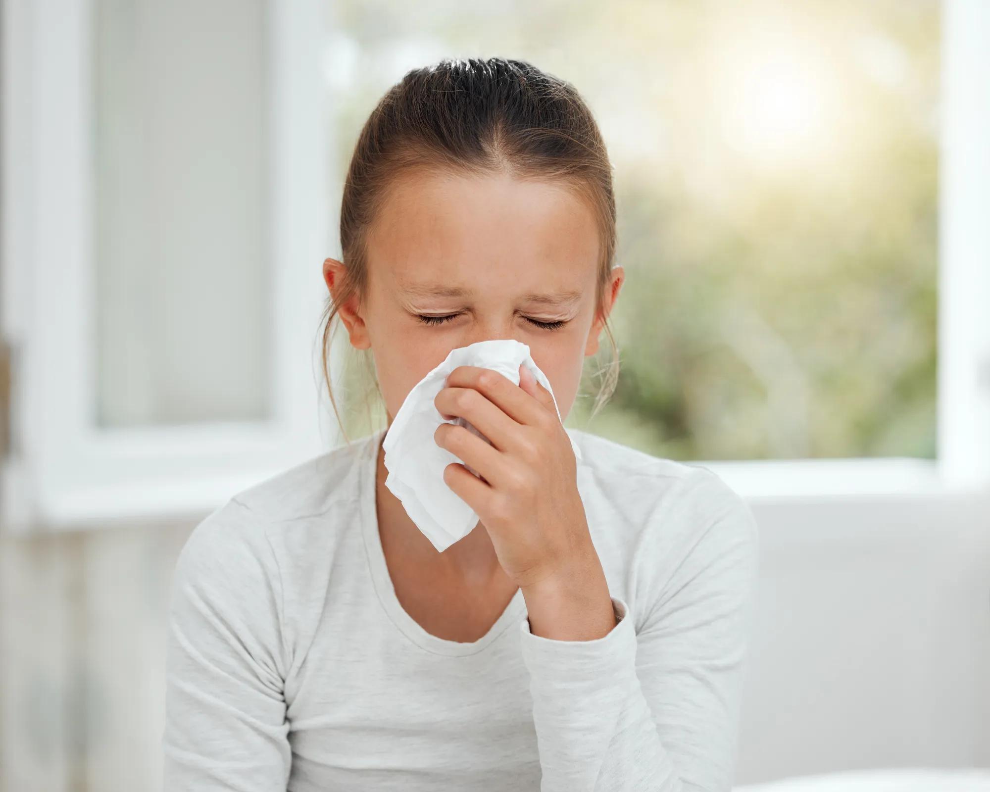 Shot of a little girl blowing her nose while sick in bed at home.