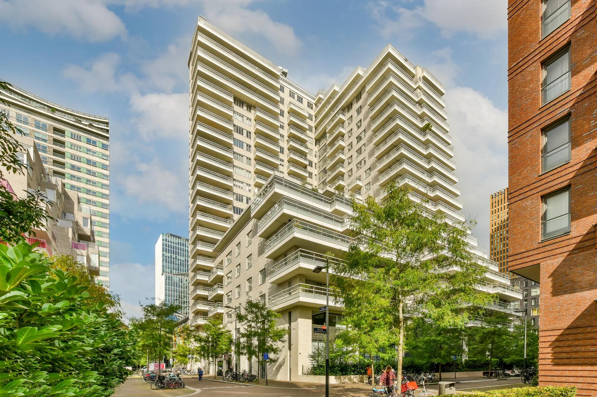 some tall buildings in the middle of an urban area with green trees and people walking on the street below them