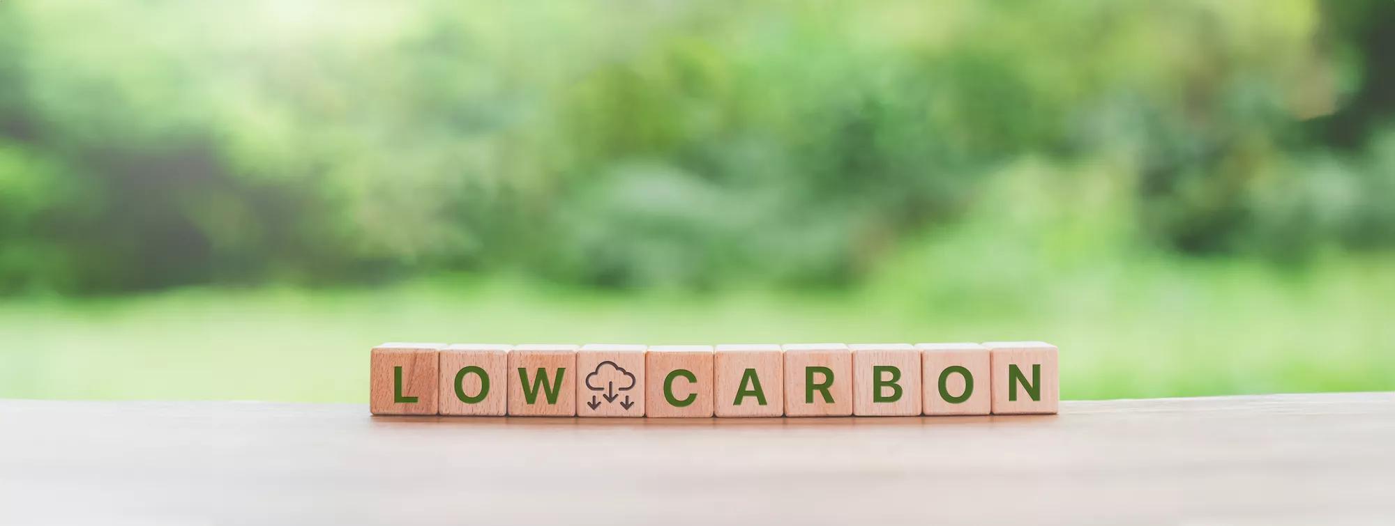 An engaging image illustrating the Low Carbon, Net Zero, and ESG (Environmental, Social, and Corporate Governance) concepts. Wooden blocks spelling out ‘LOW CARBON’ are placed on a wooden surface, symbolizing the commitment to carbon neutrality and sustainable practices. The blurred greenery in the background emphasizes the environmental aspect of these concepts.