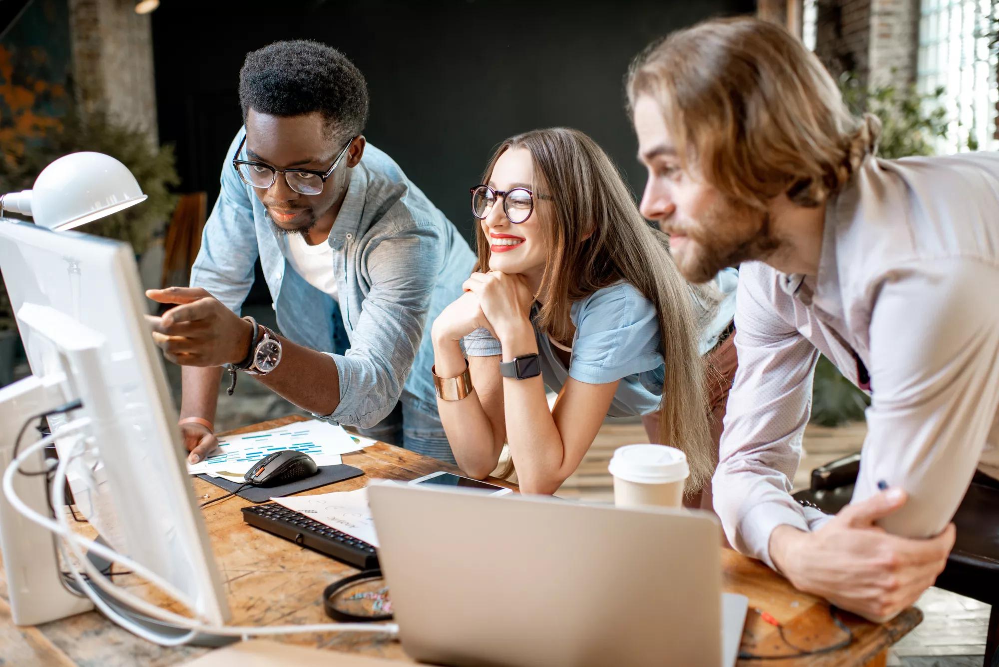 Group of young multi ethnicity coworkers dressed casually working together focused on the computer monitor indoors