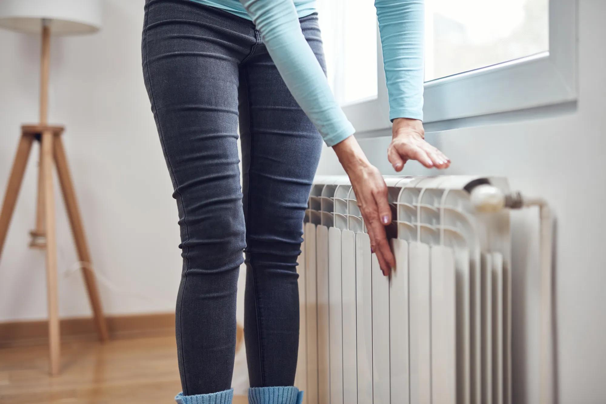 Woman heating her hands on the radiator during cold winter days.