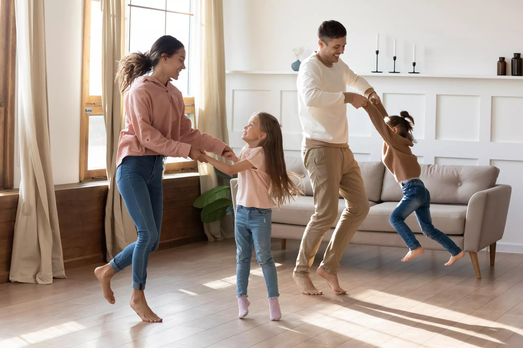 Happy young parents have fun playing with little preschooler excited daughter rest together in living room, smiling family with small kids dancing moving listen to music enjoy weekend at home