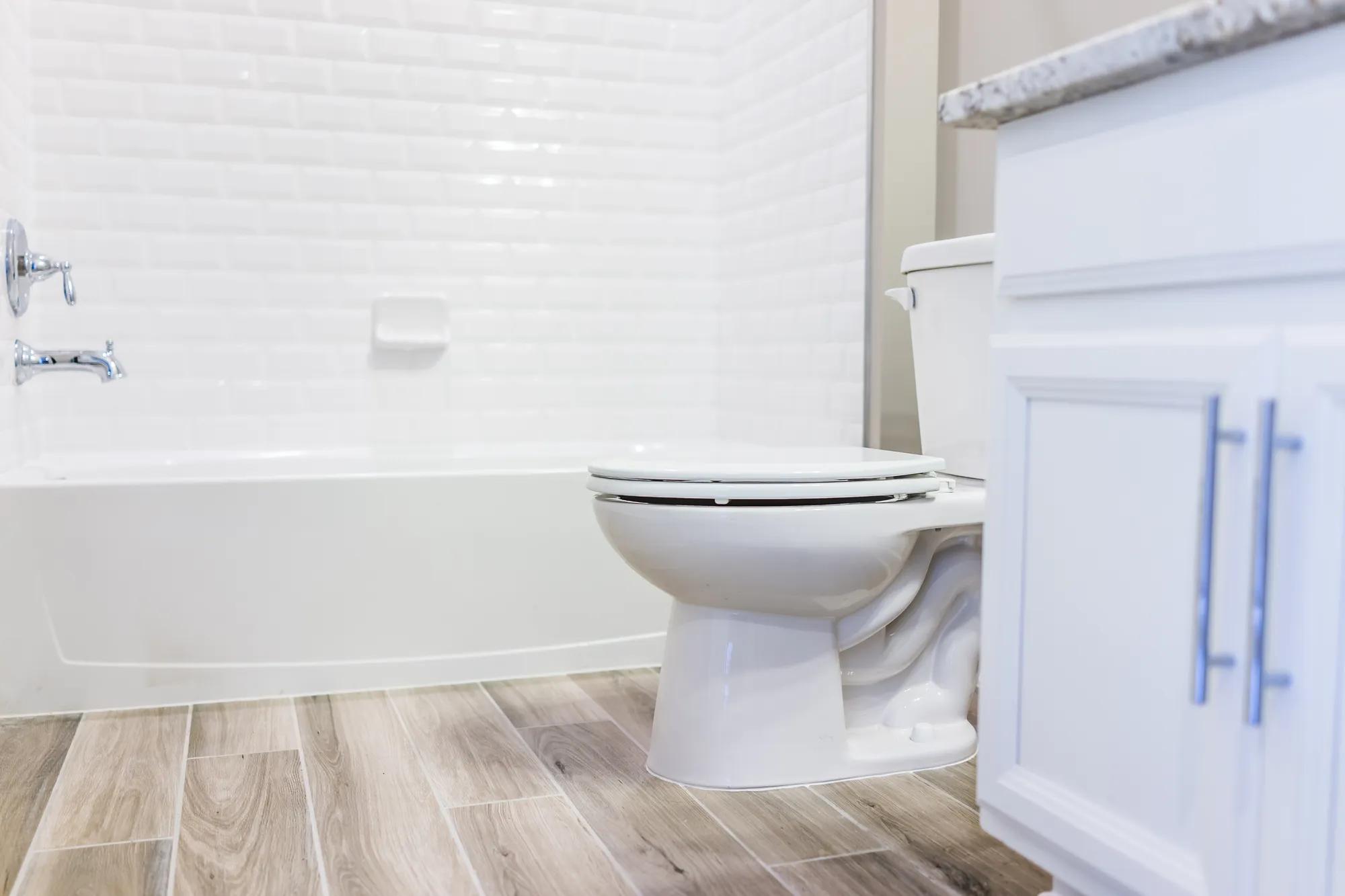 Modern white plain clean toilet bathroom, bathtub with shower tiles and hardwood floors with staging in model staging house, home or apartment