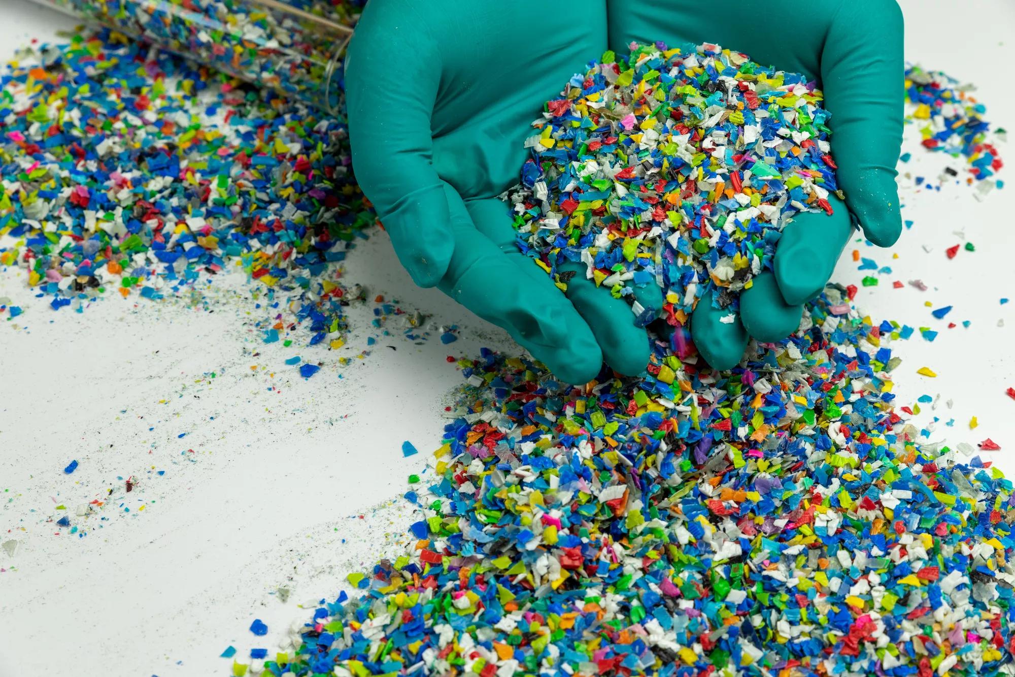 Crushed plastic on green gloved hand. Reuse of plastic. polymer beads. Scraps obtained from plastic waste. The world's plastic reduction policy. Scraps plastic on white background.