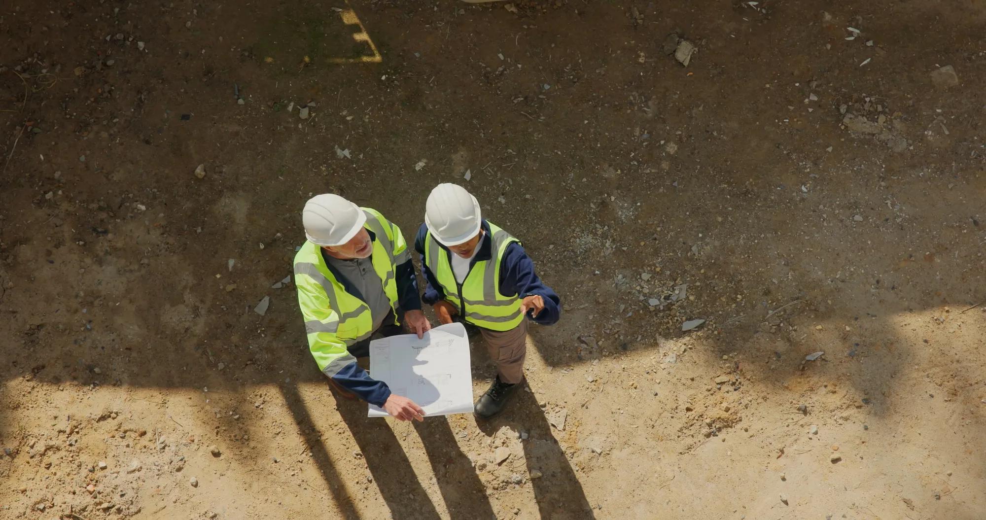 Engineering, team and outdoor with blueprint for construction plan, discussion or safety compliance. Above, space and people at site with supervisor, engineer and layout document for infrastructure