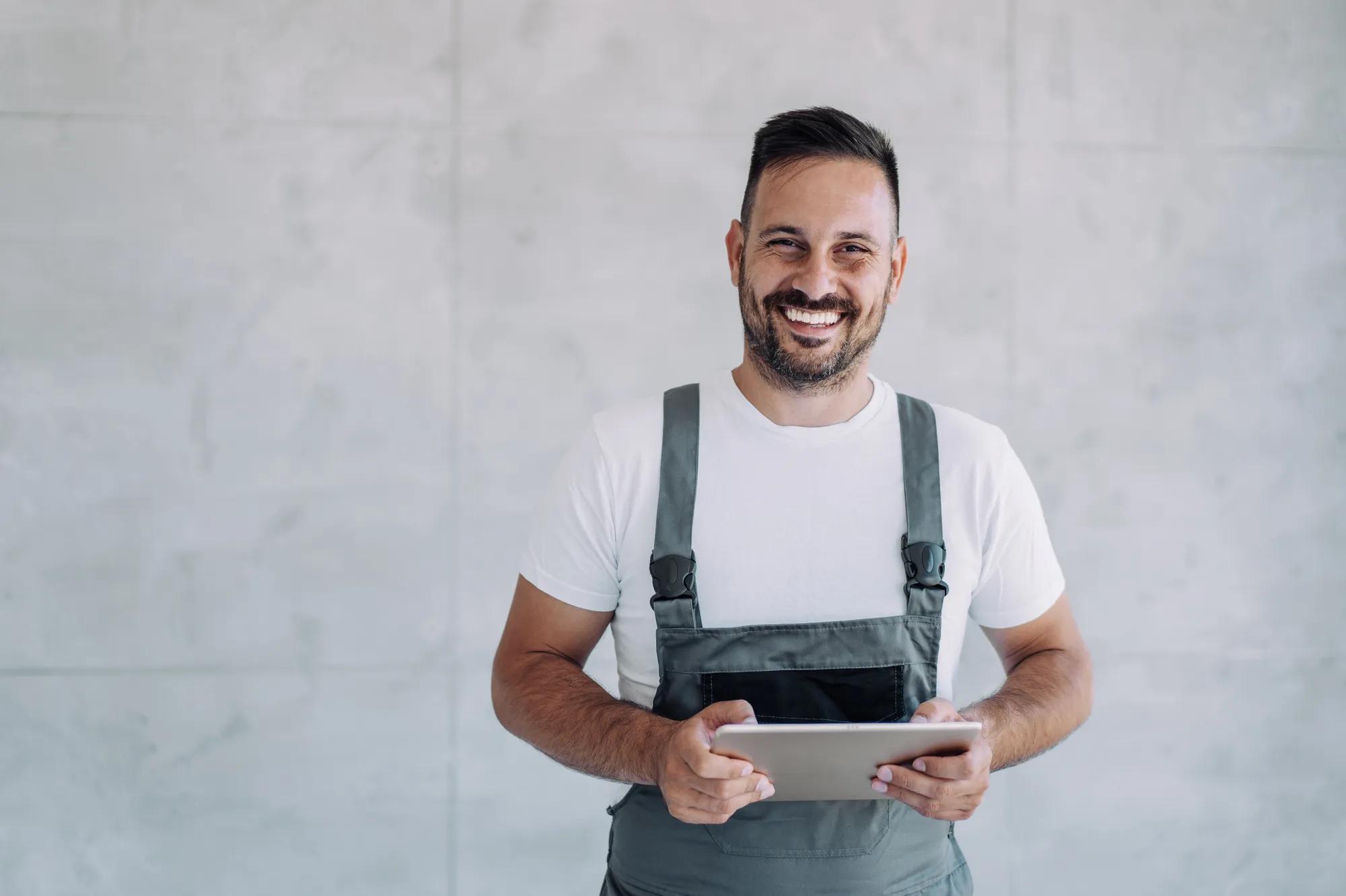 Shot of confident smiling professional handyman in overalls and white t-shirt using digital tablet.