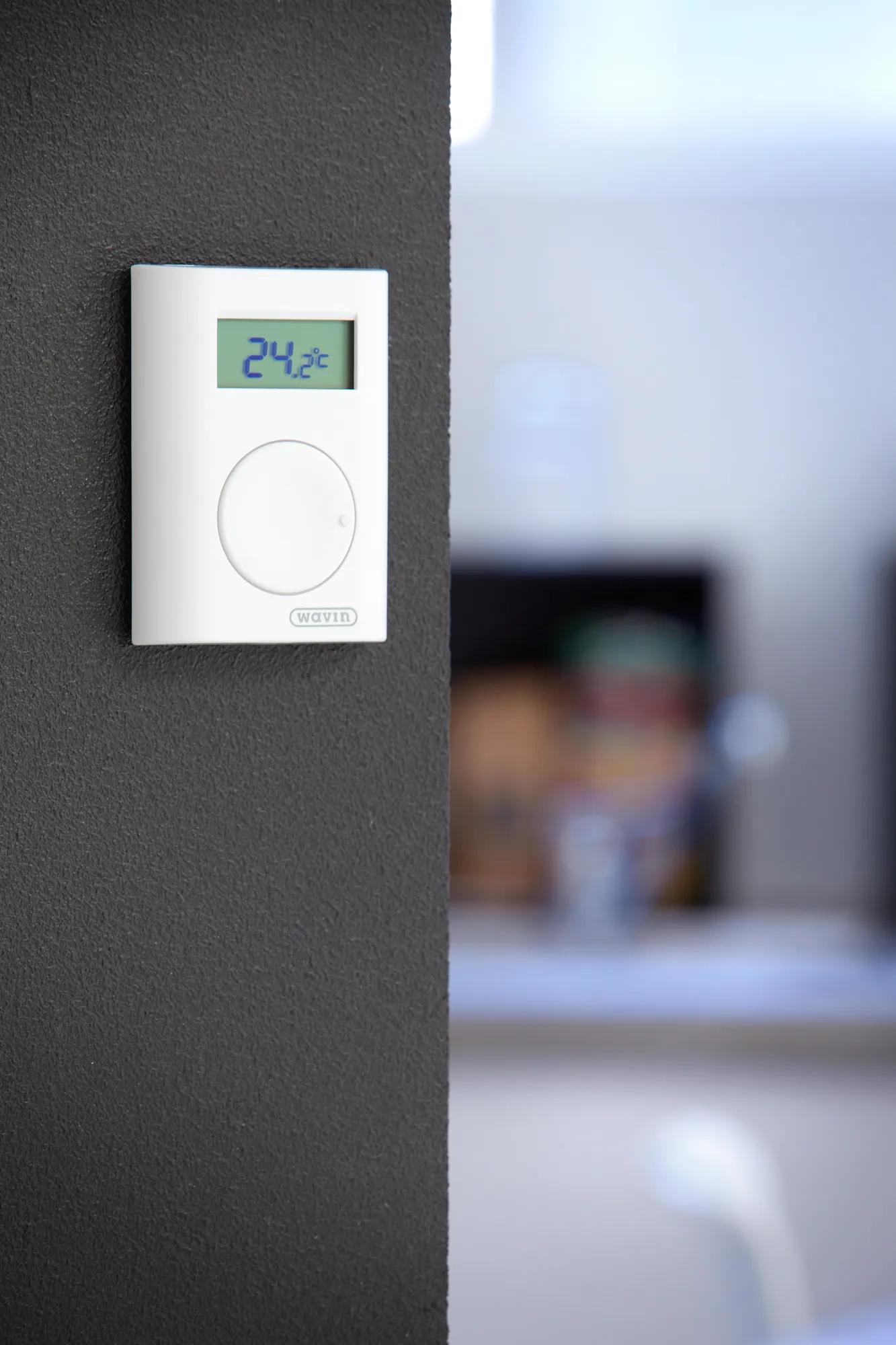 AHC 9000 room thermostat on a dark grey wall with a cozy environment in the background