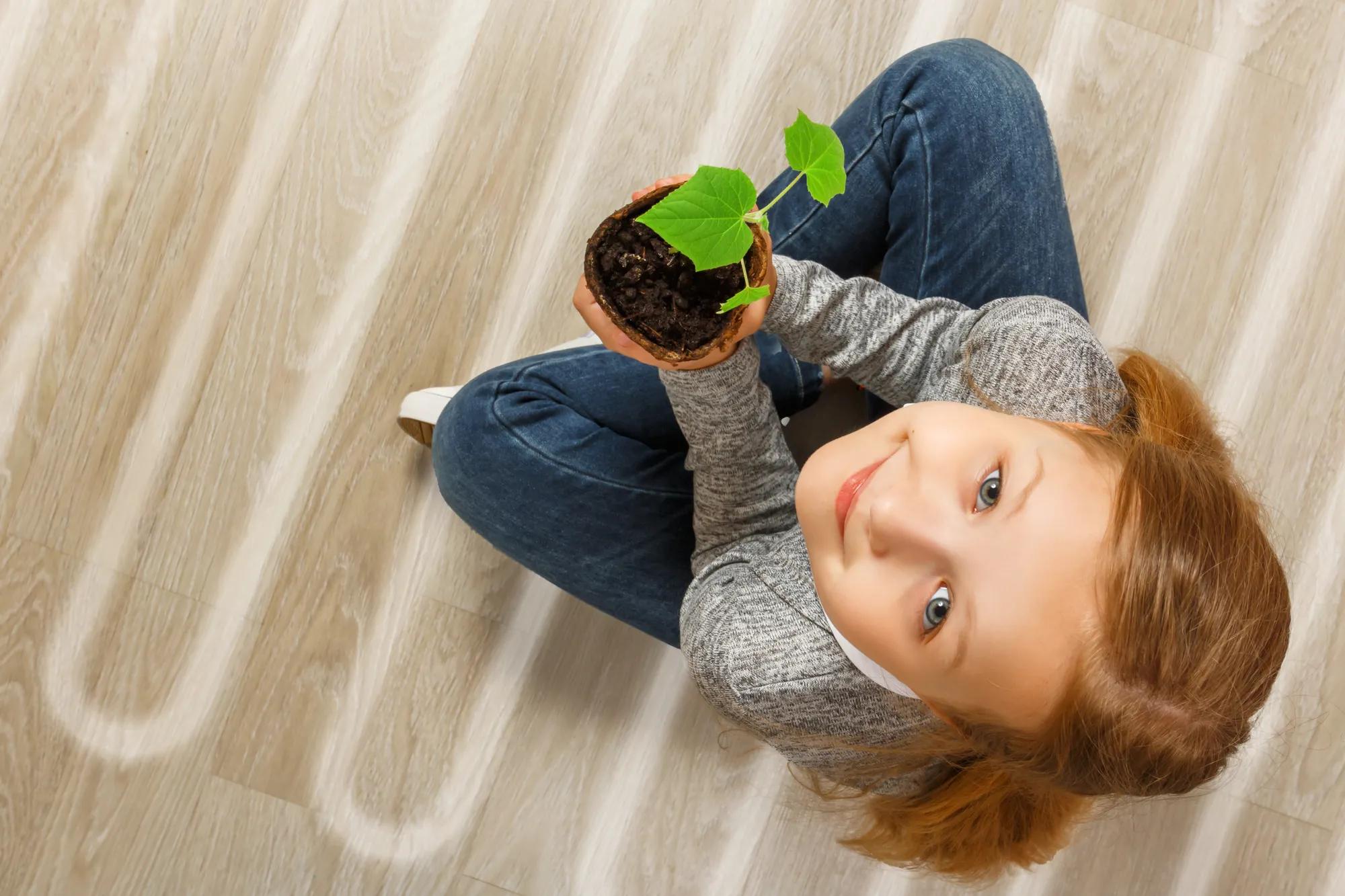 Girl sitting on floor with underfloor heating pipes visible.