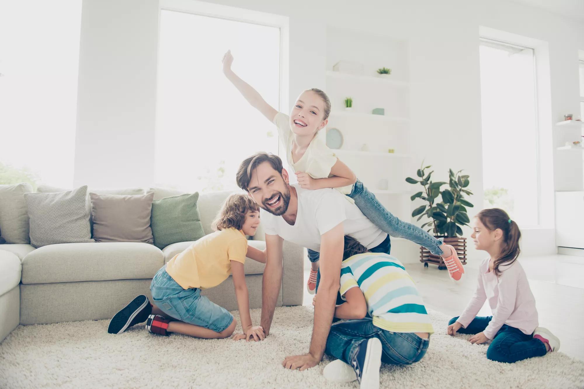 Free time, careless, carefree leisure pre-teen concept. Father spend free time with kids play near sofa in modern white light interior, ride little girl on back